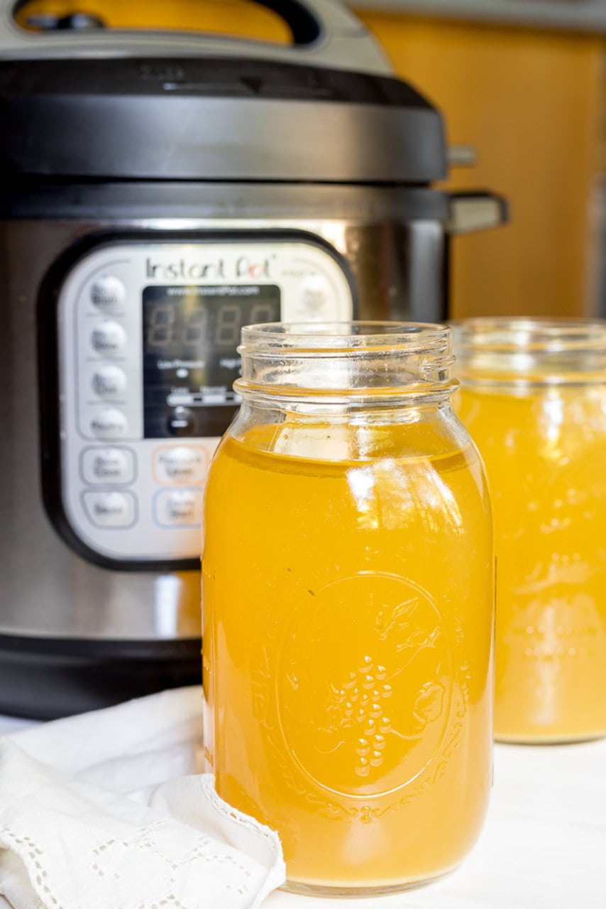 two jars filled with chicken bone broth in front of an Instant Pot pressure cooker